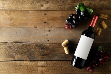 Red wine bottle with grapes and corks on brown rustic wooden table flat lay from above