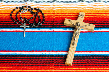 A crucifix and rosary beads on a colorful Mexican sarape.