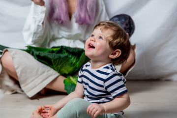 Beautiful little todler boy sitting on a floor near mother and vegetables. Healthy meal concept