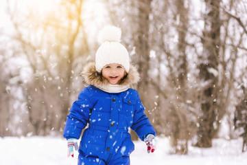 Happy laughing baby girl dressed in a blue thermal suit playing and running in a beautiful snowy winter park on Christmas