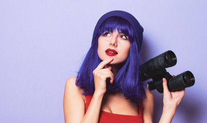 Portrait of young style hipster girl with blue hair and binoculars on purple color background