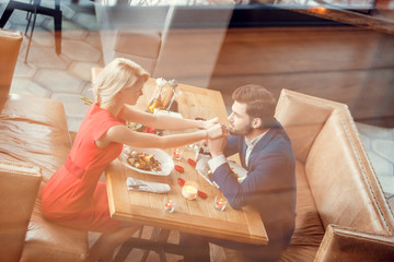 Young couple on date in restaurant sitting eating salad man kissing woman's hands joyful reflection top view