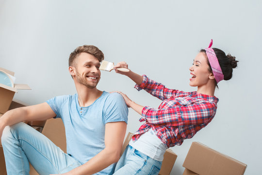 Young couple moving to new place man sitting on box looking at woman teasing him laughing happy