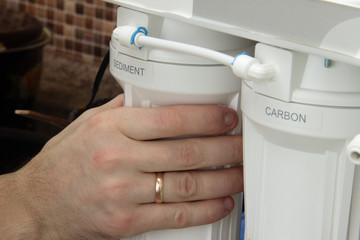 plumber change the water filter. installing osmosis in home. male hand spins the cartridge