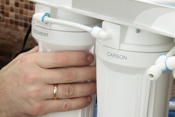 plumber change the water filter. installing osmosis in home. male hand spins the cartridge