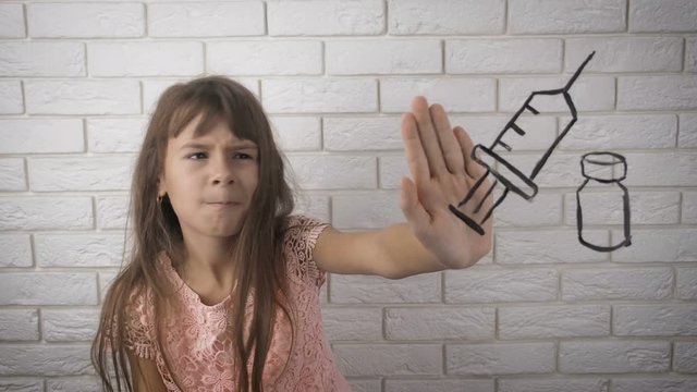 The child does not want to take medicine. No drug. Little girl shows stop gesture to the drawn syringe.