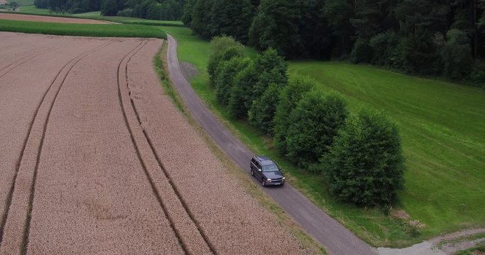 Aerial of an american SUV car driving in rural landscape throuh corn fields on a bright sunny day in bavaria germany 