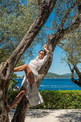 Beautiful, active, young woman in white romantic dress on olive tree, outdoor in nature. Concept: healthy life, self care, spring resolution, recreation, new beginning, nature lover, summer vibes, fun
