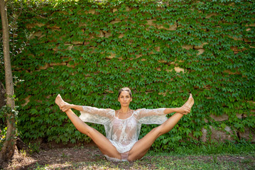 Beautiful, young woman dressed in white romantic blouse practicing yoga in nature. Concept: healthy life, self care, spring resolution, recreation, new beginning, meditation, straddle split, self love