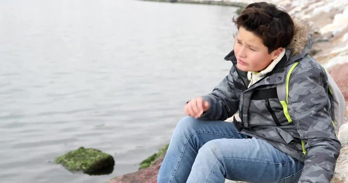 Portrait of a sad child with winter clothes sitting near the sea