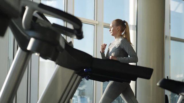 Attractive woman of middle age is running on tread mill in sport gym