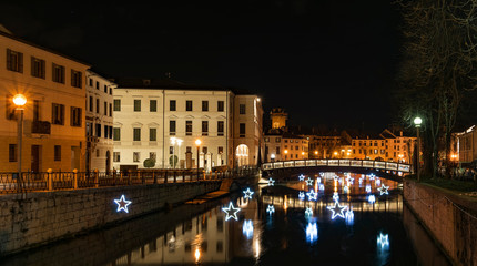 Fototapeta na wymiar 4 January 2019 Treviso (north Italy): Treviso by night during Christmas Time. the University Bridge and the light stars reflect on the river Sile. University Building on the left.
