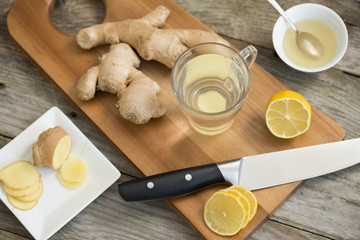 Ginger root, lemon, hot water and honey on wooden cutting board, healthy ingredients for tea against cold