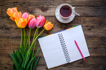 Romantic picture with tulips, tea, notebook on wooden background