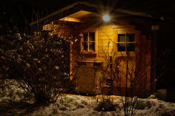 Blockhaus im winterlichen Garten, bei Dunkelheit, warmes Licht von einer Leuchte - Langzeitbelichtung