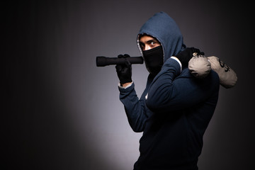 Young gangster in hood on grey background 