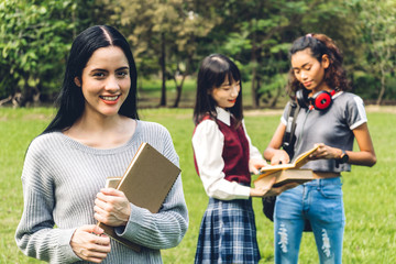 Smiling woman international students or teenagers standing and holding book smiling at camera with group of students in park at university.Education and friendship Concept