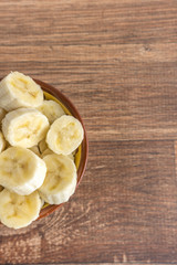 Fototapeta na wymiar Bowl with banana slices on wooden background