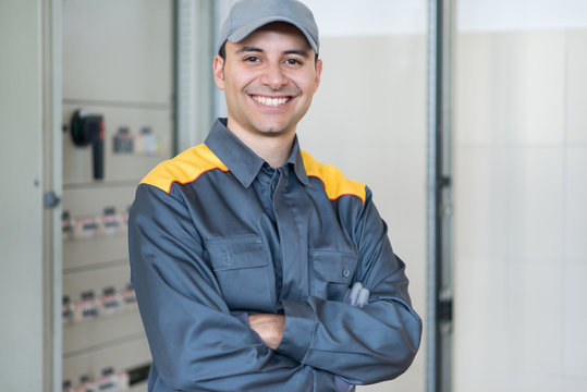 Portrait of a smiling electrician in front of an industrial electric panel in a factory
