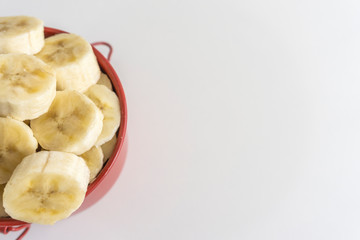 Red bowl with banana slices on white background