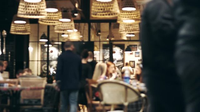 Blurred picture of the interior of a large beautiful restaurant with bright lighting. The waitress comes to the table and gives the visitors a menu and goes for drinks. Defocused restaurant