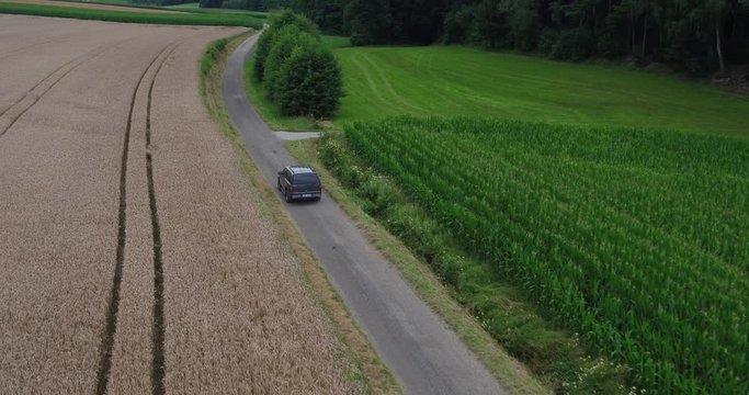 Aerial of an american SUV car driving in rural landscape throuh corn fields on a bright sunny day in bavaria germany 