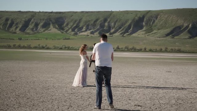 Videograph shooting video with steadicam. Young beautiful bride in a wedding dress goes to the groom. Meeting of the newlyweds outdoors