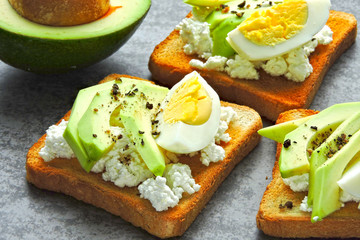 Appetizing avocado toasts with cottage cheese and quail eggs.