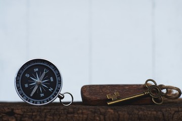 Compass and vintage key on clear white wooden wall background, vintage tone, journey planning...