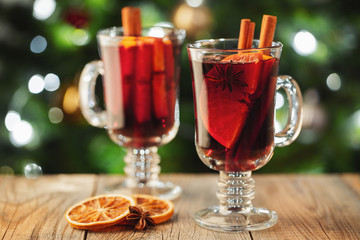 Two glass of christmas mulled wine or gluhwein with spices and orange slices on rustic table against the Christmas tree. Traditional drink on winter holiday