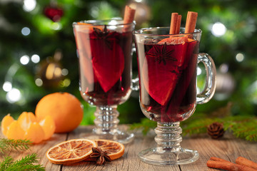 Two glass of christmas mulled wine or gluhwein with spices and orange slices on rustic table against the Christmas tree. Traditional drink on winter holiday
