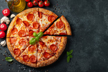 Tasty pepperoni pizza and cooking ingredients tomatoes basil on black concrete background. Top view...