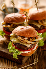 Hamburgers, homemade burgers with grilled buns with  addition of beef cutlet, fresh lettuce, tomato,pickled cucumber,  grilled onion, cheese and spicy sauce on a wooden rustic table