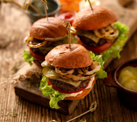 Hamburgers, homemade burgers with grilled buns with  addition of beef cutlet, fresh lettuce, tomato,pickled cucumber,  grilled onion, cheese and spicy sauce on a wooden rustic table