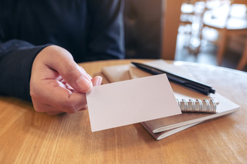 A woman holding and giving a blank empty business card to someone with notebooks on table