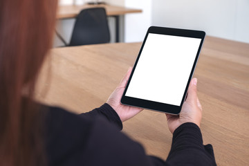 Mockup image of a woman holding and looking at black tablet pc with blank white screen while sitting in office