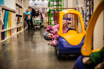 a small child plays in a baby carriage while parents choose goods in the store