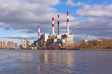Urban landscape with electric power station on a riverbank. City skyline in early morning in winter.