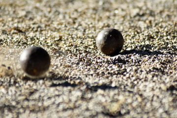 Throwing one petanque ball against another ball and impacting many other balls, until the small pebbles bounce along the impact.