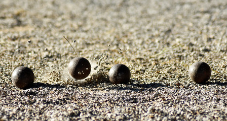 Throwing one petanque ball against another ball and impacting many other balls, until the small pebbles bounce along the impact.
