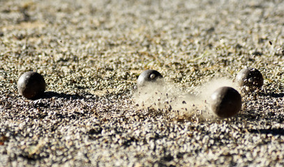 Throwing one petanque ball against another ball and impacting many other balls, until the small pebbles bounce along the impact.