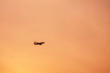 Airplane flying in warm tone sunset sky on cloudy day