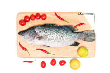 Fresh raw Asian Sea Bass fish  on wooden cutting board with lemon, tomato and chilli on white background, top view. Seafood asian cooking ingredients.