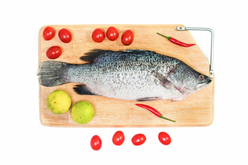 Fresh raw Asian Sea Bass fish  on wooden cutting board with lemon, tomato and chilli on white background, top view. Seafood asian cooking ingredients.