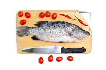 Fresh raw Asian Sea Bass fish  on wooden cutting board with chilli, tomato and knife on white background, top view. Seafood asian cooking ingredients.