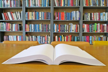 The old book open on the wooden table in the library. Selective focus with blurred bookshelves background. Education and book's day concept.