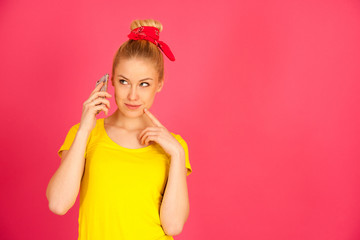 cut teenage woman in yellow t shirt talks on smart phone  over pink bacckground