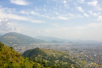 Fototapeta premium view of the city in a green mountain valley in the mist under the blue sky and white clouds