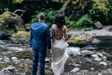 Naklejka na ściany i meble bride and groom standing on rocks near stream in forest