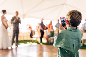 young boy holding a smart phone taking a picture of a bride and groom on their wedding day